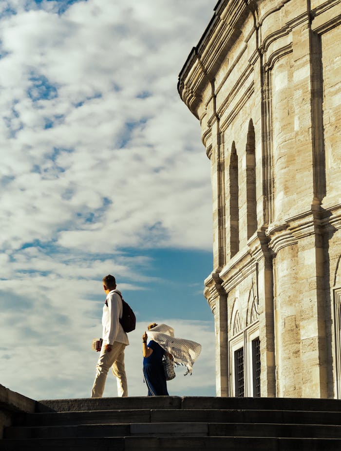 services-01 Two people walk by an ornate building under a vibrant blue sky, capturing historical elegance.