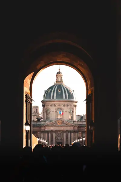 hero-img-01 Dramatic view of the Institut de France framed by an archway in Paris, capturing a vibrant historical atmosphere.