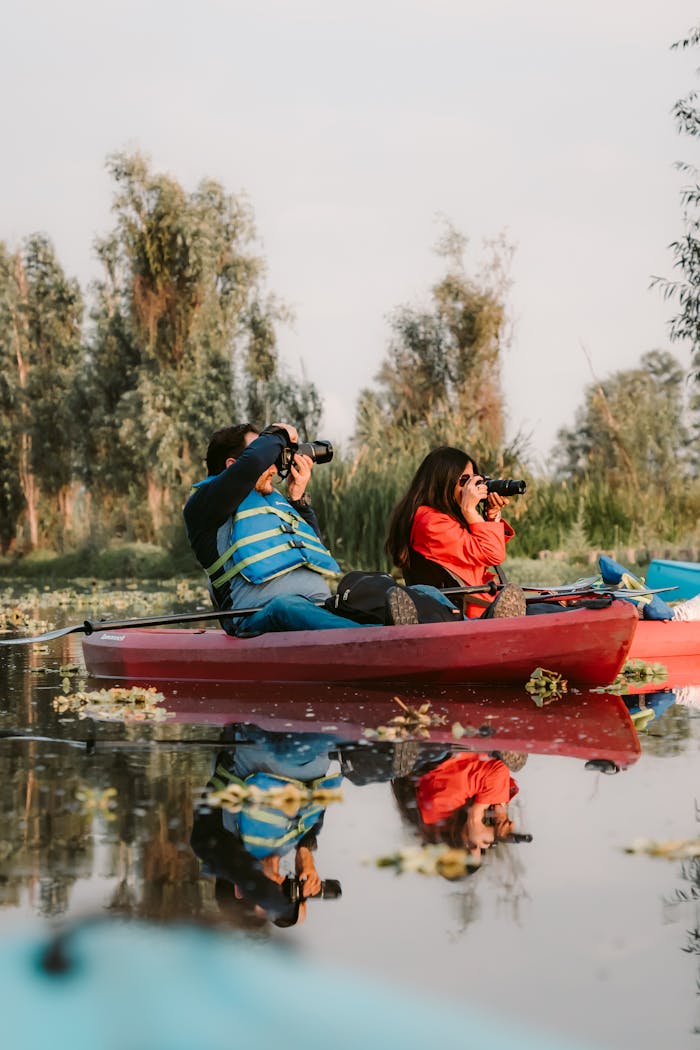 contact-img Two adults kayaking on a calm lake with cameras, capturing natures beauty. Perfect leisure activity.
